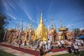 Buddhist people praying and walking around a golden pagoda.